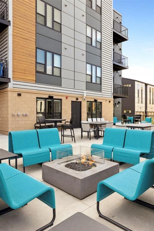 a patio with blue chairs and a fire pit in front of a building