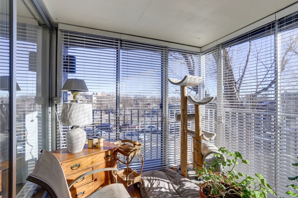 a living room with a large window with blinds and a desk with a chair