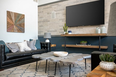 A living room with a black couch, a round table, and a flat screen TV mounted on the wall.