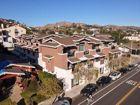 A residential street with houses on both sides and cars parked on the side of the road.