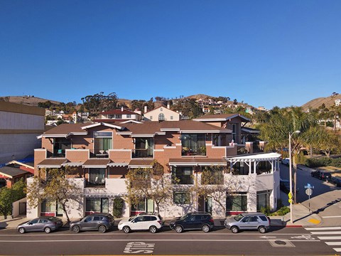 A building with a white facade and a brown roof with a parking lot in front of it.
