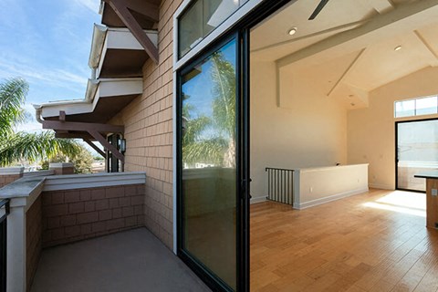A balcony with a glass door leading to a room with wooden floors.