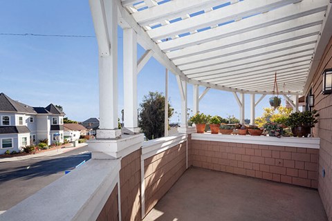 A patio with a white roof and pillars with plants on the windowsill.