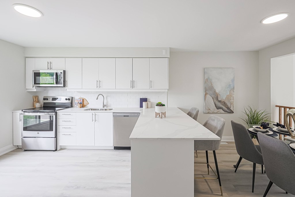 A modern kitchen with a white island and grey chairs.