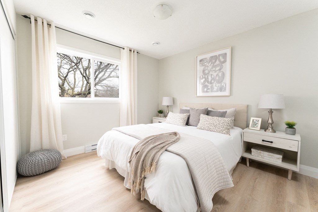 a bedroom with a large window and a bed with a white comforter and pillows