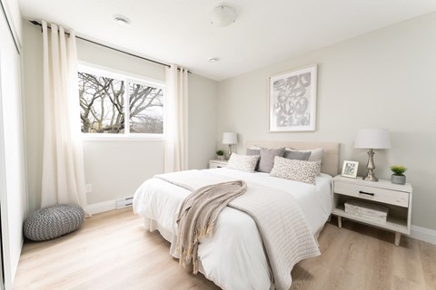 a bedroom with a large window and a bed with a white comforter and pillows