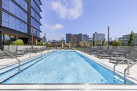 a swimming pool with lounge chairs next to a building with a city in the background