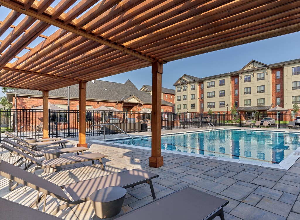 A wooden pergola shades a swimming pool and lounge chairs.