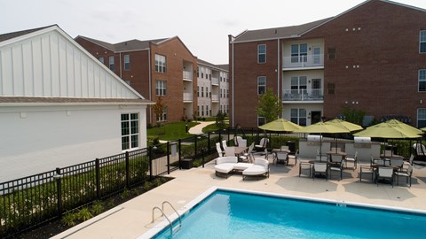 A pool surrounded by chairs and umbrellas in front of apartment buildings.