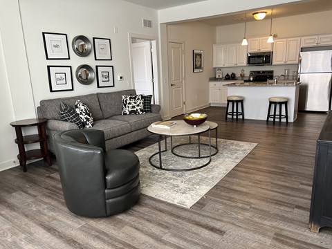 A grey couch with a black leather chair and a small table in a room with wooden flooring.