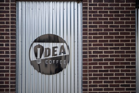 A sign for IDEA COFFEE is on a corrugated wall.
