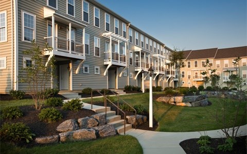 A row of apartment buildings with a stone wall and steps leading to the front doors.