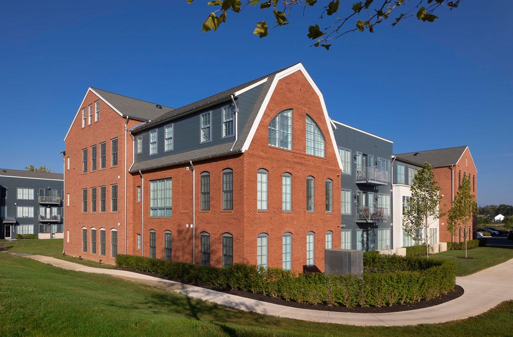 A red brick building with a black roof and a white building with a black roof in the background.