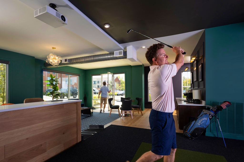 A man is playing golf in a room with a green wall.