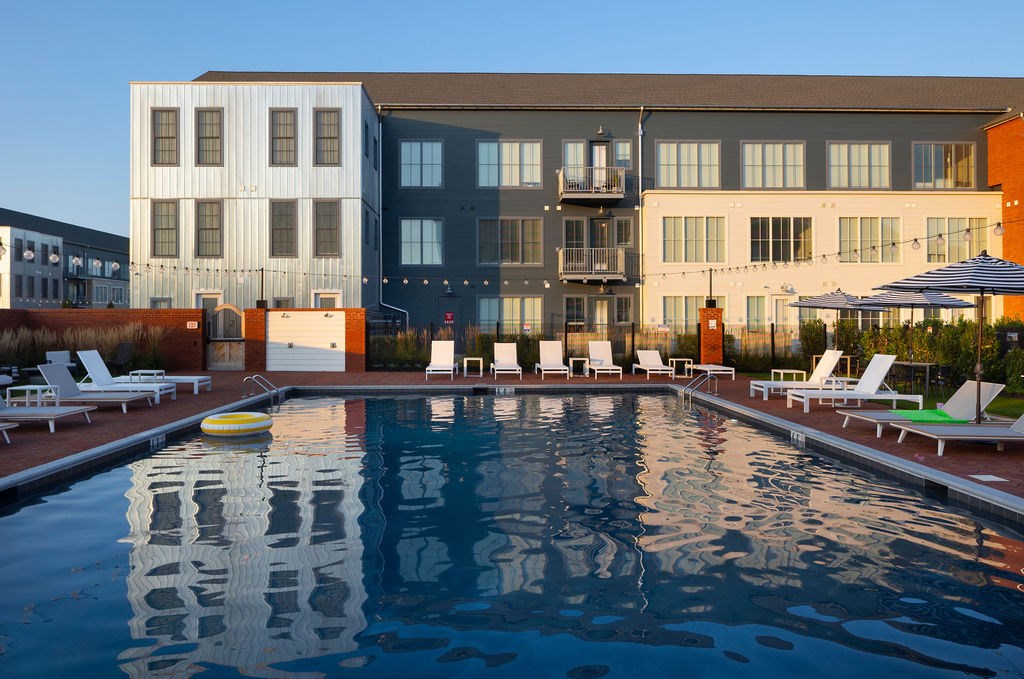 A large swimming pool in front of a building with lounge chairs around it.
