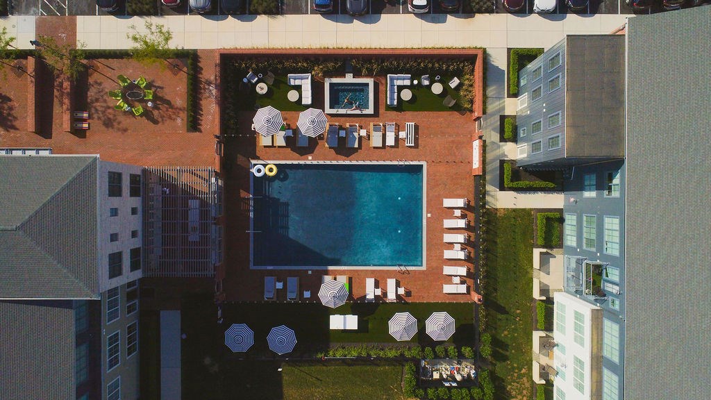 A pool surrounded by a patio with chairs and umbrellas.