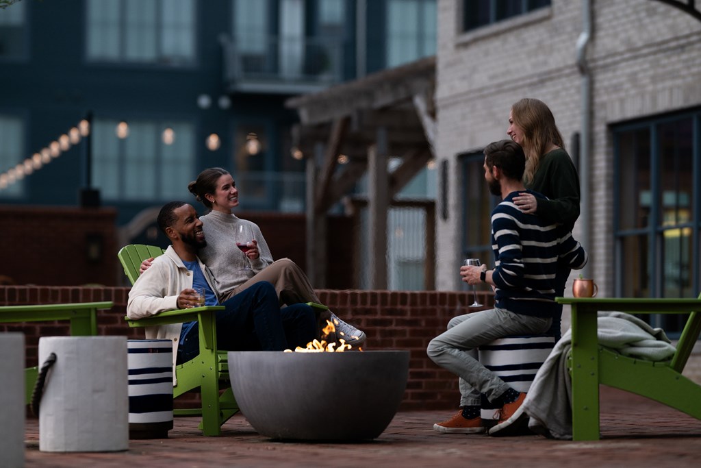 Three people sitting around a fire pit on a patio.