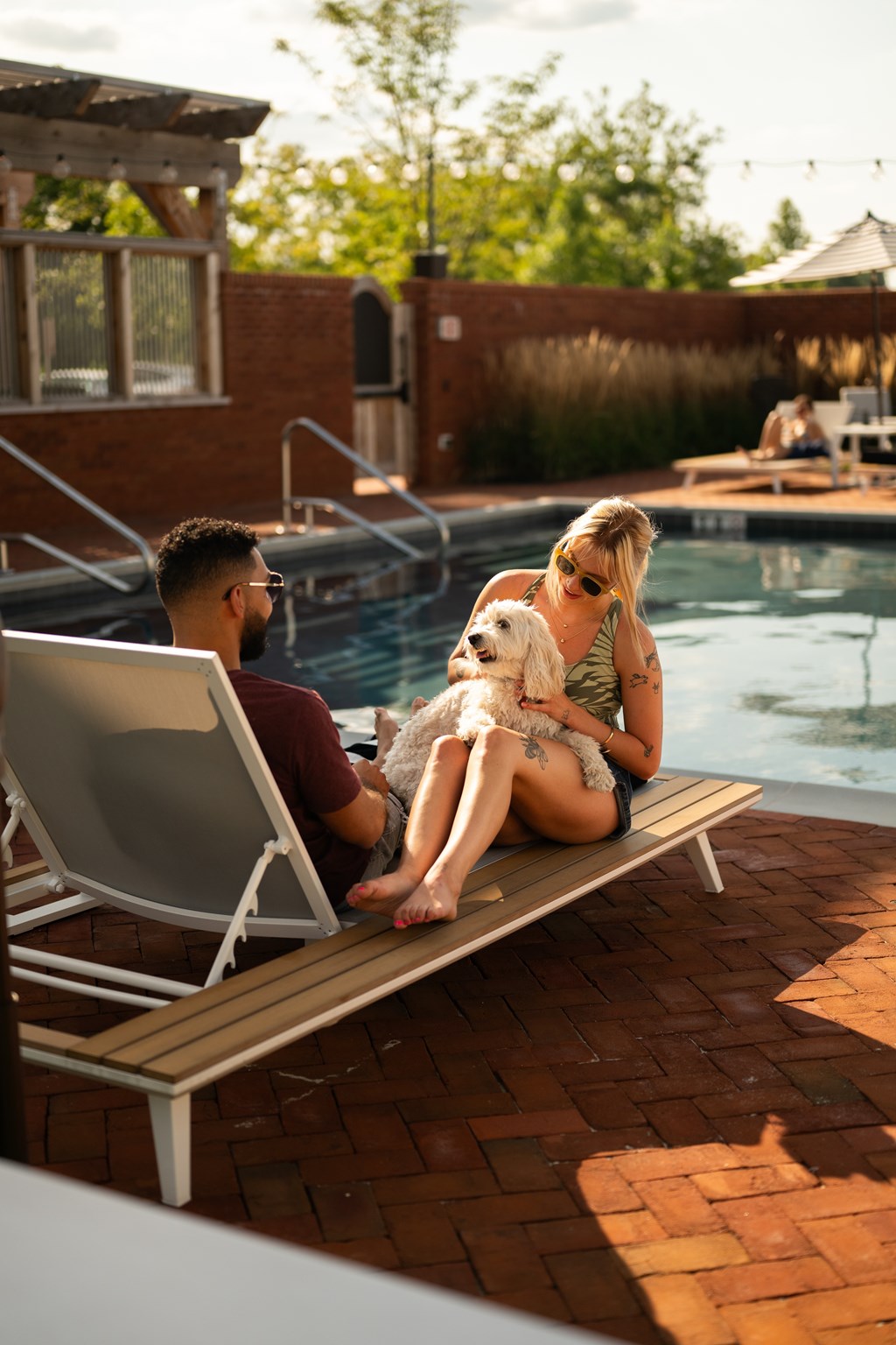 A man and a woman are sitting by a pool with a dog.