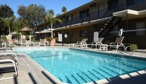 A swimming pool with sun loungers and a building in the background.