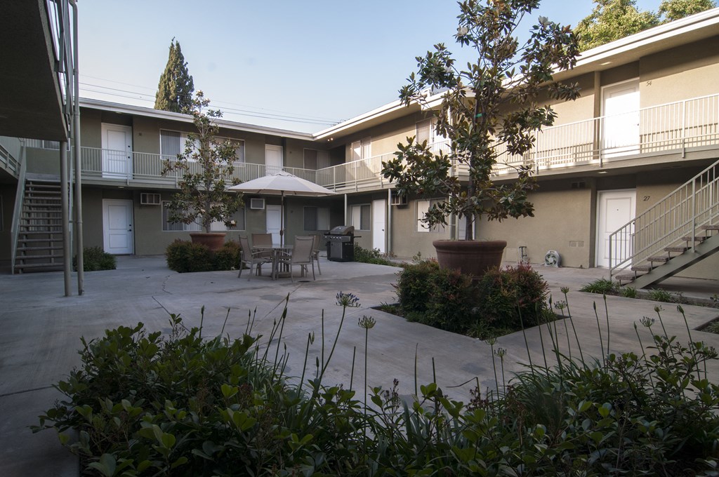 a courtyard with tables and chairs and trees in front of a building