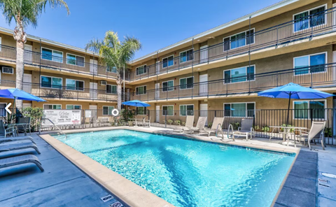 A swimming pool in front of a building with lounge chairs and umbrellas.