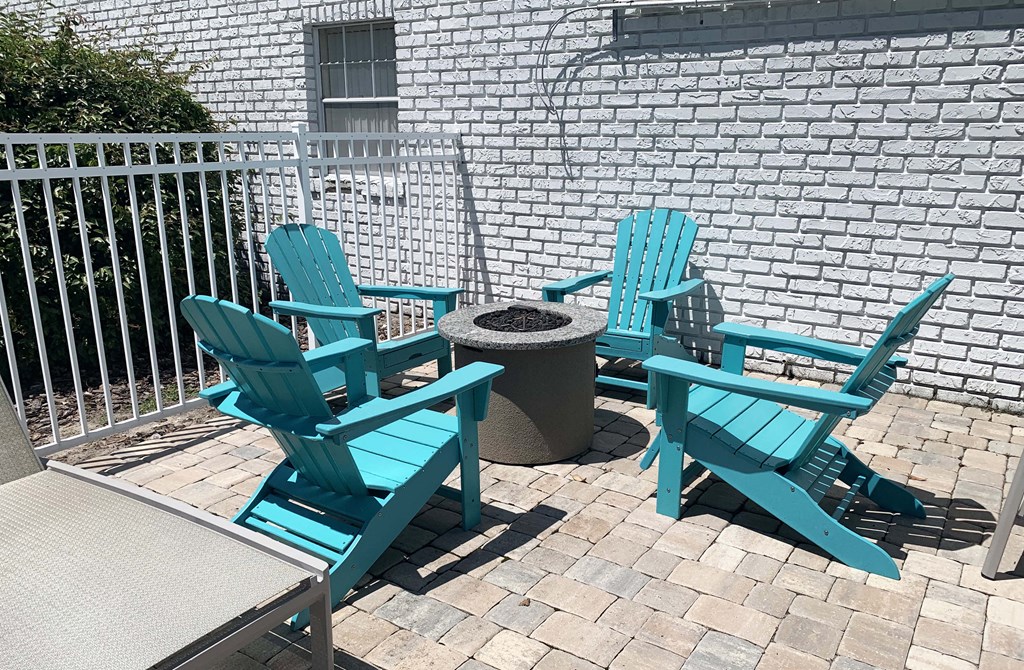 a patio with blue adirondack chairs and a fire pit