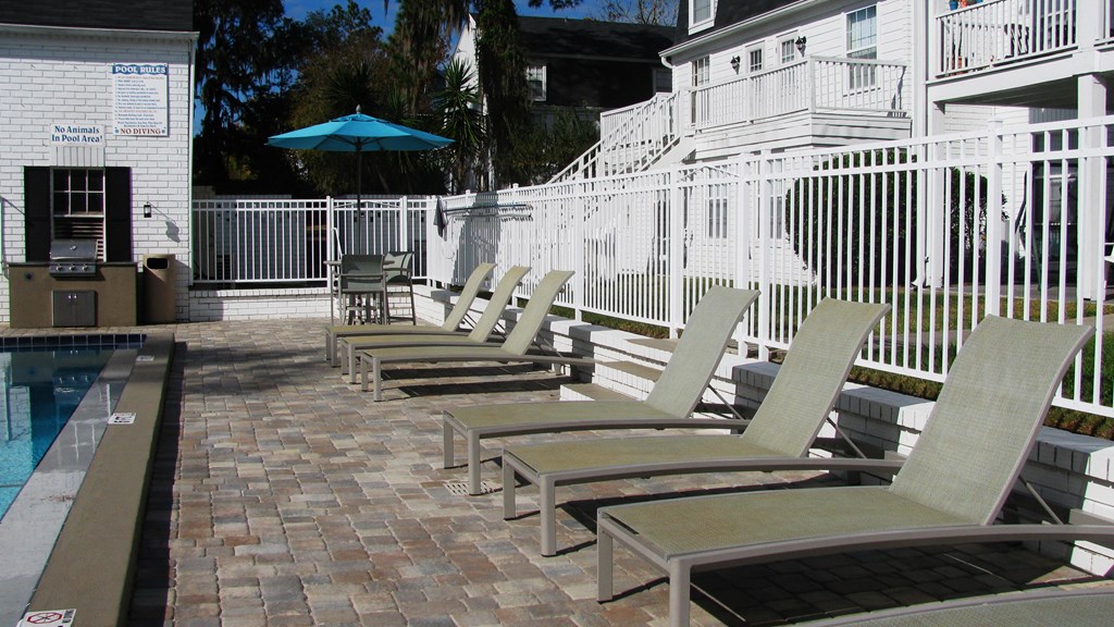 a row of chaise lounges on a brick patio next to a pool