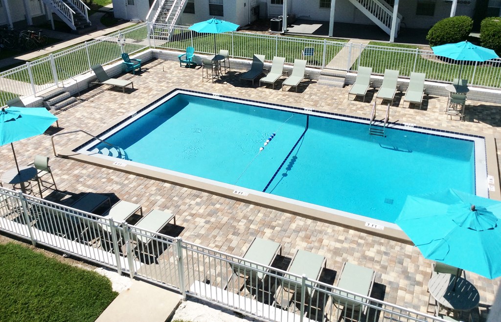an aerial view of a resort style pool with lounge chairs and umbrellas