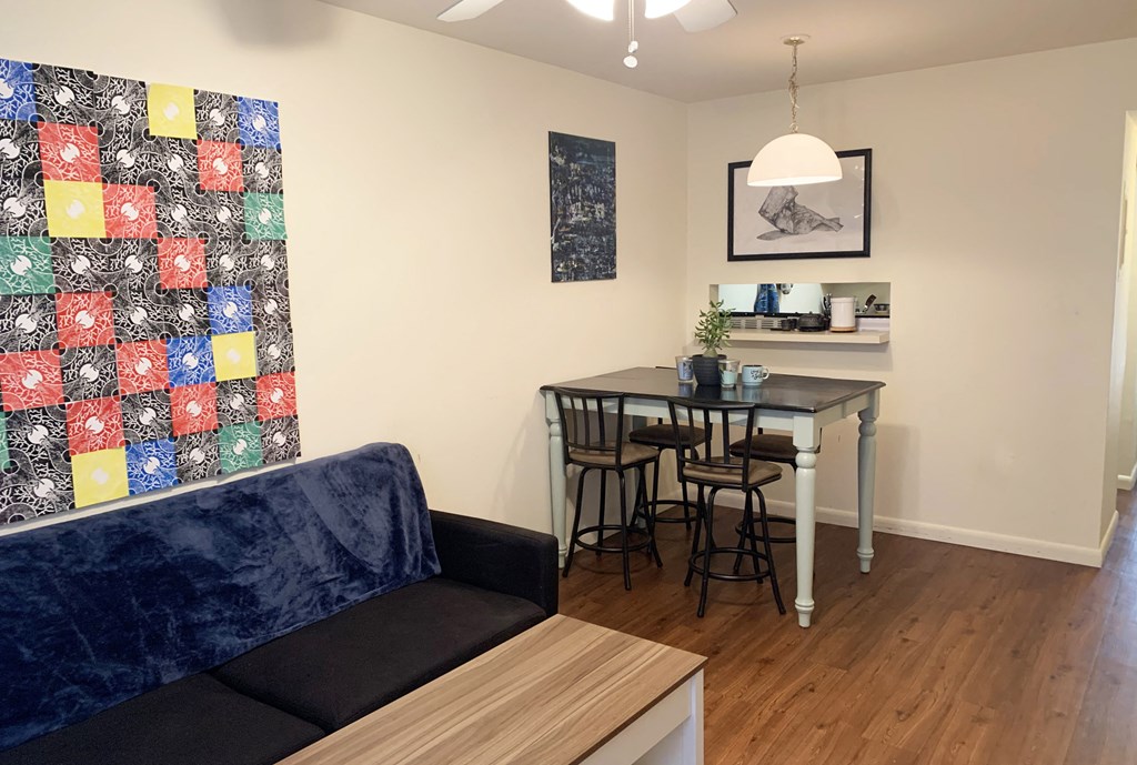 a living room with a couch a table and chairs and a quilt on the wall