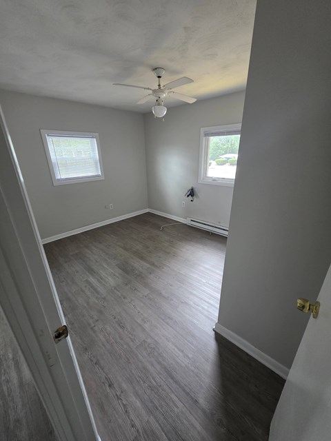 A room with a ceiling fan and two windows.