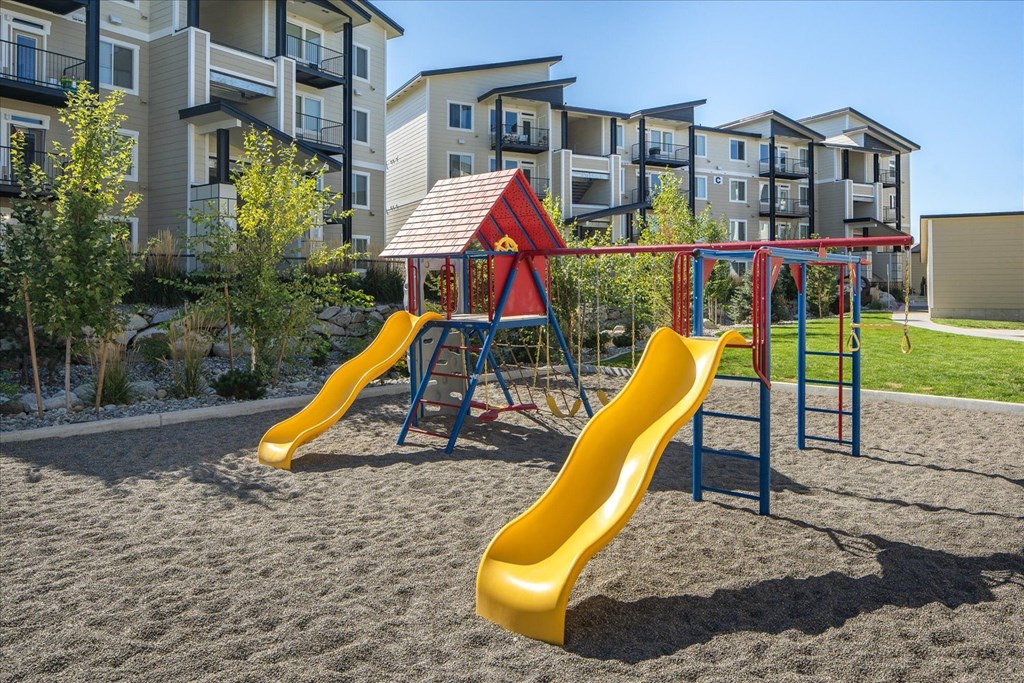 a playground with slides and a swing set in front of an apartment building