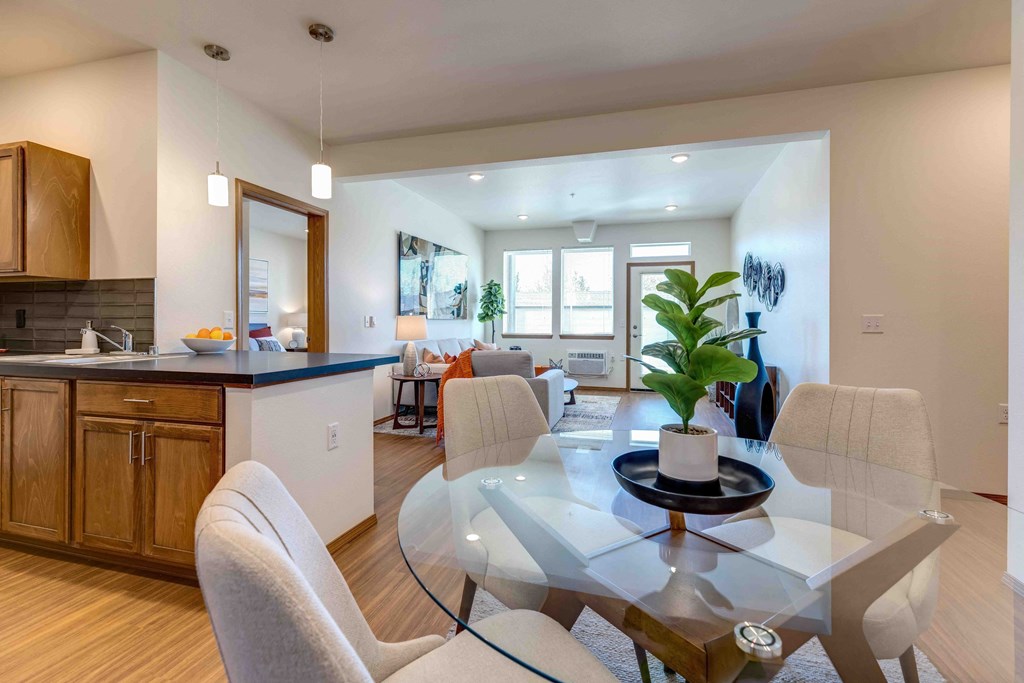 a dining area with a glass table and chairs and a kitchen in the background