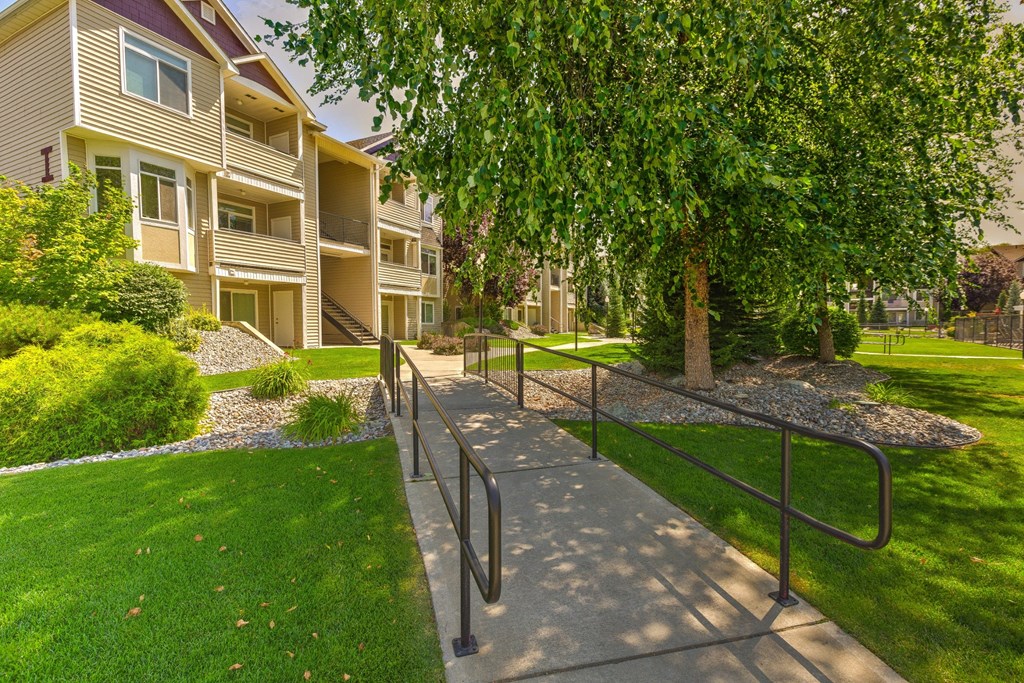 an apartment building with a sidewalk and tree in front of it