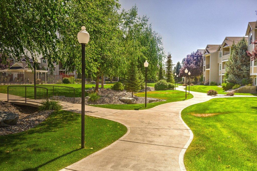 a pathway through a park with trees and buildings in the background