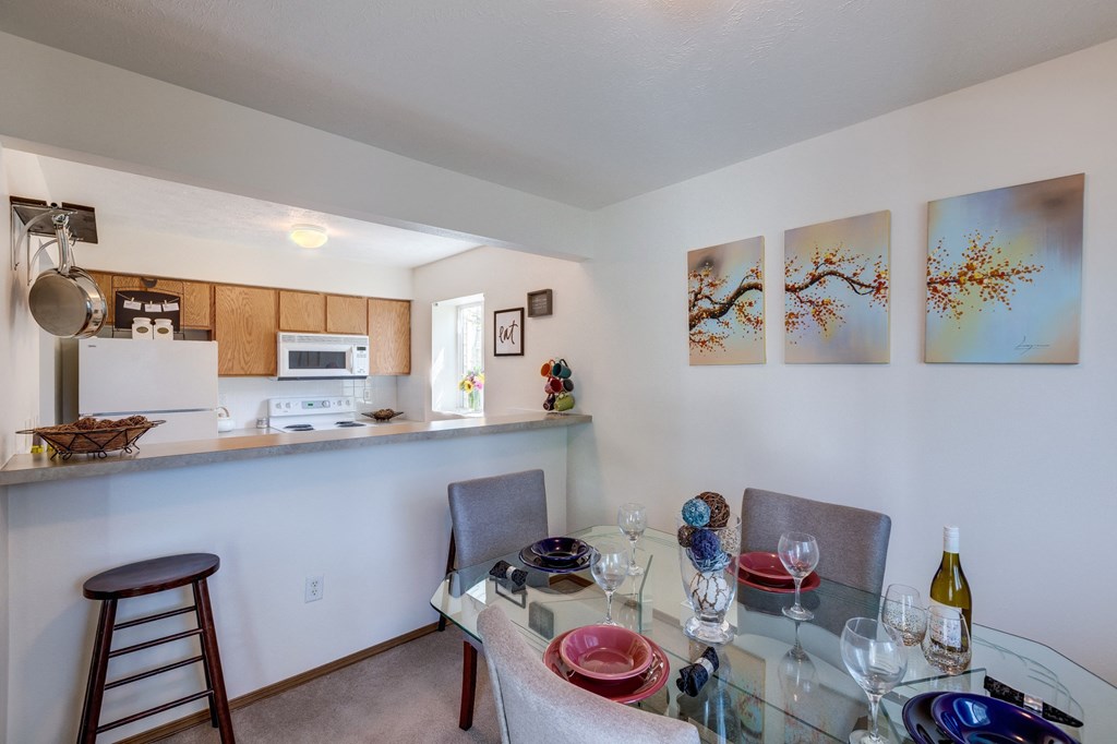 a dining area with a glass table and chairs and a kitchen in the background