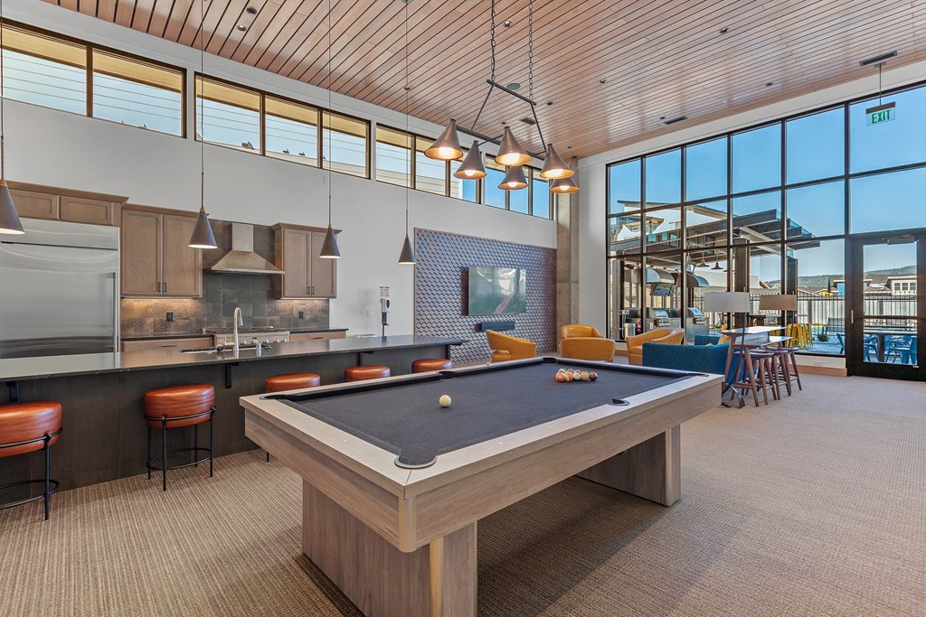 a pool table in a clubhouse with a kitchen and bar