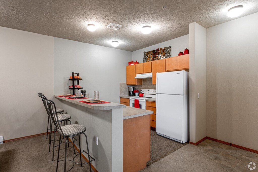 A kitchen with a white refrigerator freezer next to a counter top with three stools