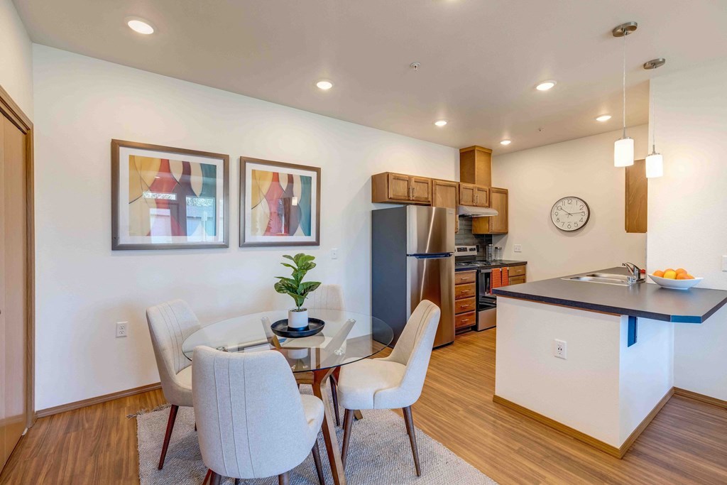 a dining area with a glass table and chairs and a kitchen in the background