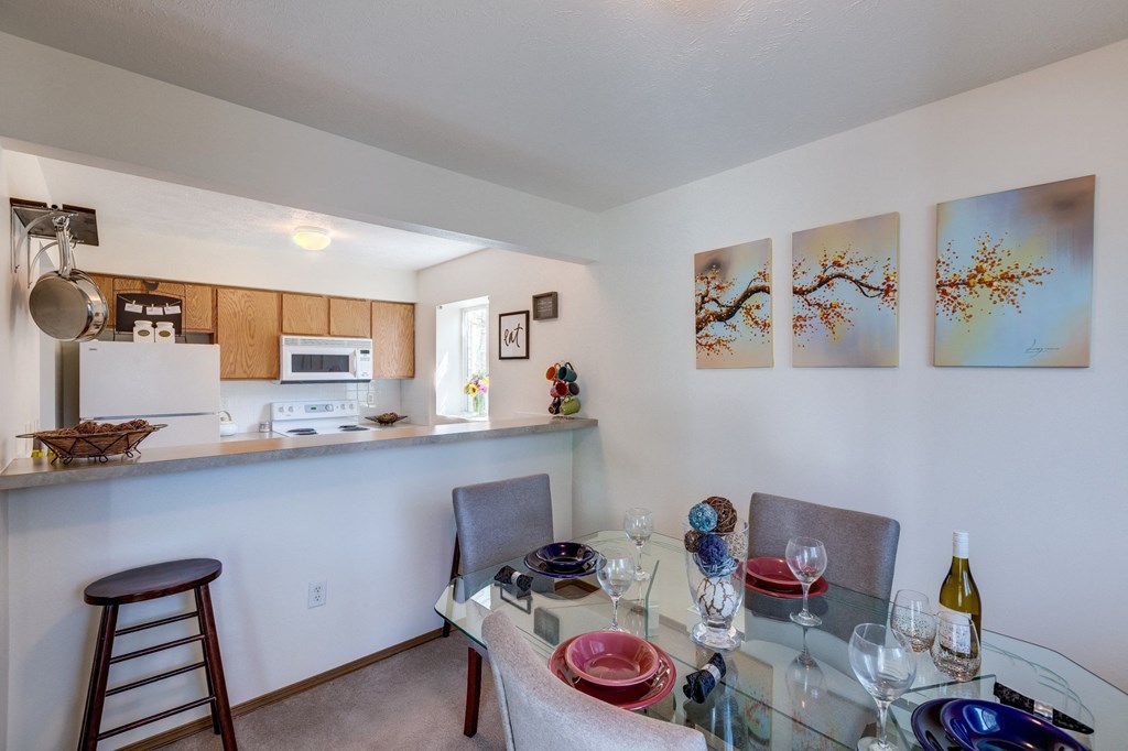 a dining area with a glass table and chairs and a kitchen in the background