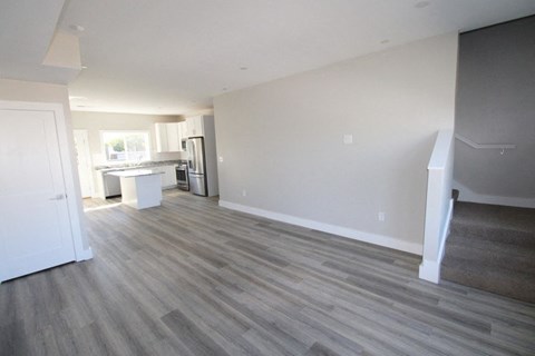 A room with a kitchen area in the background and a staircase on the right.