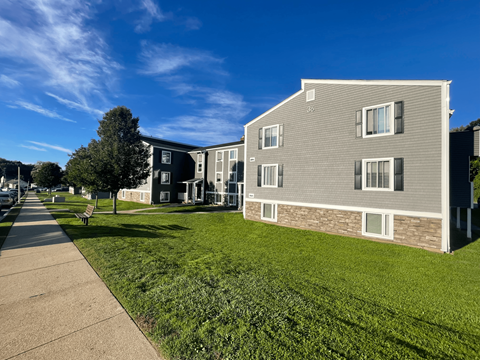 an apartment building with a green lawn and a sidewalk