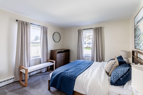 A bedroom with a bed, nightstand, and window with curtains.