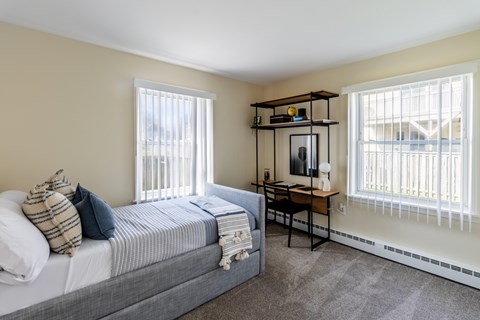 A bedroom with a bed, desk, and window.