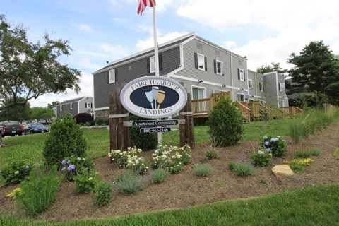 the sign in front of an apartment building with a flag and flowers