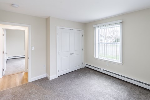 A room with a carpeted floor and a window with blinds.