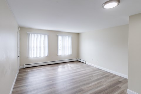 A room with wooden flooring and two windows.
