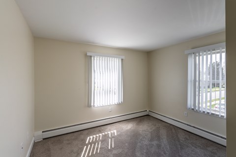 A room with a carpet and a window with blinds.