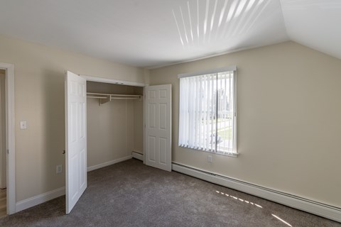A room with a carpeted floor and a window with blinds.