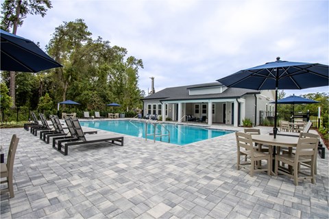 A pool area with a table and chairs and umbrellas.