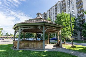 A gazebo with a brown roof is surrounded by a grassy area.